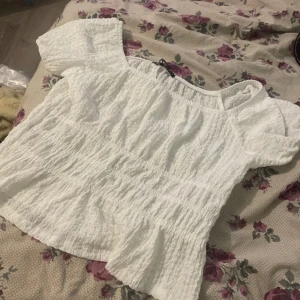 Vit  blus från Sinsay - Superfin vit blus från Sinsay i storlek S. Med korta ärmar och har en smockad, rynkad struktur som ger en cool och luftig känsla. Perfekt till jeans eller kjol för en fräsch look. Helt ny med prislapp!🩷