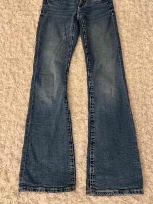 Lågmidjade bootcut jeans från Gina Tricot  - Säljer dessa blåa jeans från Gina Tricot med lågmidja, två knappar fram och visa sömmar. 