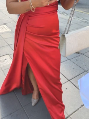 Röd långklänning med slits - Säljer en elegant röd långklänning i vacker chiffong. Klänningen är använd endast vid ett tillfälle, och bilderna är tagna vid detta tillfälle. Nedtill finns en lätt smutsrand eftersom klänningen var nära marken, men detta går enkelt att tvätta bort. Köpt för 5 000 kr. Strl. Xs-S