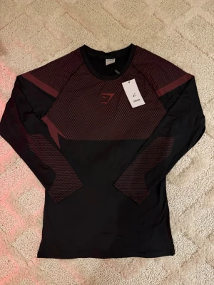 Gymshark Onyx V5 Långärmad Träningströja – Svart & Röd - Gymshark Onyx V5 Långärmad Träningströja – Svart & Röd 👕 Storlek: M 🎨 Färg: Svart med röda detaljer 🧵 Modell: Onyx V5 – långärmad funktionsplagg ✨ Skick: 10/10 – helt ny, aldrig använd 🏷️ Detalj: Originaltag kvar 💎 Märke: Gymshark
