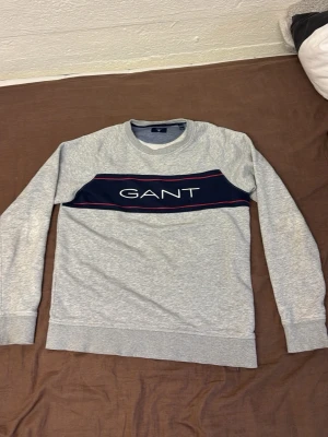 Grå tjocktröja från GANT. - En snygg tjocktröja från GANT i färgen grå. Bra skick men har slitits lite oåvarmen som visas i sista bilden.