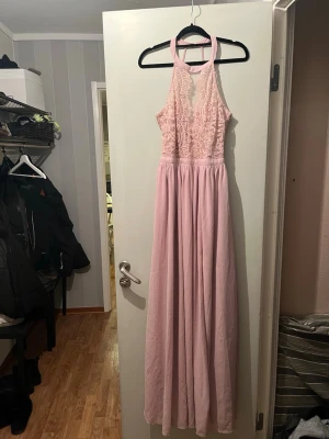 Ljusrosa långklänning från NLY Eve - Säljer en elegant ljusrosa långklänning från NLY Eve i storlek 34. Klänningen har spetsdetaljer upptill, hög halsringning och är ärmlös med snygg ryggdesign. Perfekt för speciella tillfällen!
