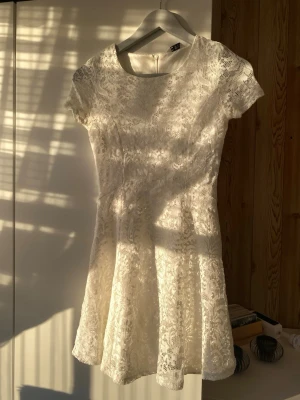 Studentklänning - Säljer en söt vit kortklänning från H&M med spetsdetaljer och rund hals. Klänningen har korta ärmar och ett fint, feminint fall. Perfekt för dig som gillar romantisk stil och vill ha något ljust och fräscht i garderoben.