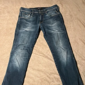Replay Hyperflex jeans blå W31 L32 - Säljer ett par Replay Hyperflex jeans i blå tvätt med snygga slitningar och kontrastsömmar. Modellen har klassisk femficksdesign, raka ben och normal passform. Materialet är stretchigt jeans för extra komfort. Perfekt för dig som gillar stilrena och bekväma jeans. Litet hål vid högra knät.