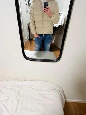 Beige pufferjacka med dragkedja - Säljer en beige pufferjacka med huva och dragkedja framtill. Jackan har en quiltad design och är perfekt för kyliga dagar. Den har en clean look och passar dig som gillar stilrena och enkla plagg. Snygg att matcha med jeans eller sneakers.