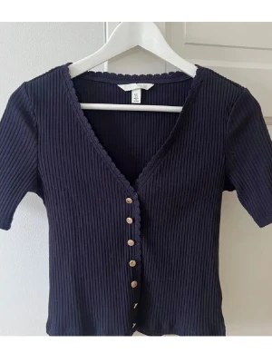 Mörkblå ribbad topp med knappar - Säljer en mörkblå ribbad topp från HM med v-ringning och knappar framtill.
