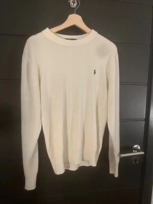 Vit stickad tröja från Polo Ralph Lauren - Säljer en vit stickad tröja från Polo Ralph Lauren med klassisk rund hals och diskret logga broderad på bröstet. Tröjan har långärmad passform och är gjord i mjukt bomullsmaterial som känns skönt mot huden. Perfekt för dig som gillar stilrena och enkla plagg. Plagget är perfekt till nu till vintern samt att plagget är vit/beige och är väldig stilig. Plagget passar M samt S