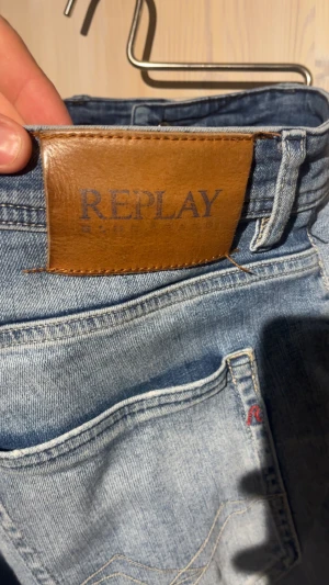 Replay ljusblå jeans med slitningar - Säljer ett par ljusblå jeans från Replay med snygga slitningar och råa, fransiga benslut. Jeansen har klassisk femficksdesign, knapp och dragkedja fram samt Replay-logga på bakfickan och insidan. Tillverkade i bomull med en skön passform.