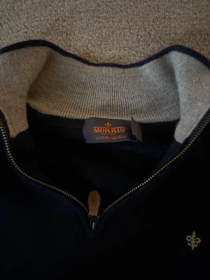 Marinblå half zip tröja Morris - Snygg marinblå tröja från Morris i 100% merinoull med half zip och kontrastfärgad krage i grått. Liten broderad logga på bröstet och läderdetalj på dragkedjan. Perfekt för dig som gillar stilrena och klassiska plagg.