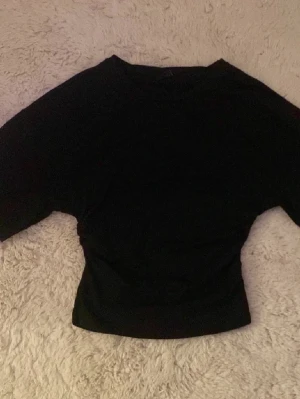 Svart topp med snörning från Gina Tricot - Säljer en svart topp från Gina Tricot i storlek S. Toppen har lång ärm och snygg snörningsdetalj på sidan som ger en cool och modern look. Materialet är mjukt och stretchigt, perfekt att styla med jeans eller kjol.