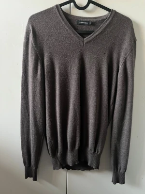 Brun v-ringad tröja från J.Lindeberg - Mjuk och stilren brun v-ringad tröja från J.Lindeberg i storlek S, passar xs. Tröjan har långa ärmar och ribbade muddar vid ärmslut och nederkant. Perfekt för dig som gillar klassisk och enkel design med diskret logga på bröstet.
