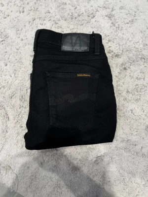 Svarta Nudie Jeans Skinny 28/30 - Svarta jeans från Nudie Jeans i slim fit med klassisk femficksdesign och snygga svarta sömmar på bakfickorna. Modellen har normal midja och är tillverkad i mjukt jeansmaterial med stretch för extra komfort.