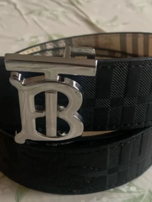 Svart och beige rutig Burberry-väst - Säljer en stilren väst från Burberry med klassiskt rutigt mönster i beige, svart och rött. Västen har en snygg form och är tillverkad i skinn med inslag av textil. Perfekt för dig som vill ha en ikonisk look med lyxig känsla och tydlig logodetalj framtill.