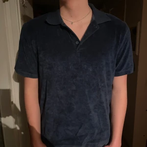 Mörkblå polotopp från Jack & Jones - Säljer en mörkblå polotopp från Jack & Jones Premium. Toppen har korta ärmar, klassisk krage och knappar vid halsen. Materialet är mjukt och har en frottéliknande känsla som gör den extra skön att bära. Perfekt för dig som gillar stilrena och bekväma plagg.