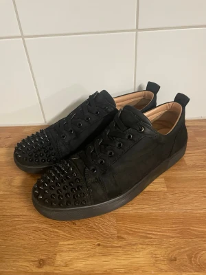 Svarta sneakers med nitar från Louboutin - Säljer ett par svarta sneakers från Louboutin i svart med spikar storlek 41 allt är original inget fel på dom. Säljer dom för de är för små nu. Nypris 8000kr mitt pris 1200. Såklart äkta. Svarar på alla frågor.