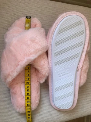 Nya Puderrosa fluffiga tofflor i storlek Medium -  mått se bilder  - Supermjuka och fluffiga sandaler från VORA i en ljus puderrosa färg. De har korslagda band och en platt sula i syntet med räfflad undersida. Perfekta för att glida runt hemma och ge dina fötter extra mysfaktor.