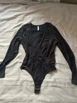 Svart body - Svart body från Chiara Forthi med glittrigt tyg och omlott-design framtill. Långärmad och med tryckknappar, super bra till t.ex nyår