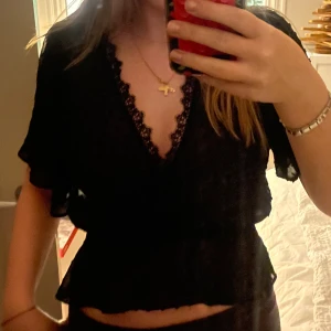 Svart prickig blus från Zara - Säljer en svart blus från Zara perfekt till fester och middagar, i storlek M men är lite mindre i storleken. Blusen är transparent med prickigt mönster, har omlott-design och spetsdetaljer vid halsen. Modellen är luftig med korta ärmar och resår i midjan💕