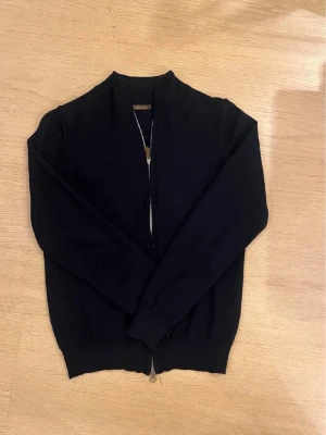 Mörkblå kofta från Stenströms - Snygg mörkblå kofta från Stenströms med hel dragkedja framtill och ribbad krage. Tröjan är långärmad och har ribbade muddar vid ärmslut och nederkant. Materialet är mjukt och stickat, perfekt för kyliga dagar.