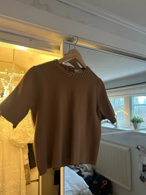Brun topp från Zara med kedjedetalj - Säljer en brun topp från Zara med korta ärmar och guldiga detaljer. 