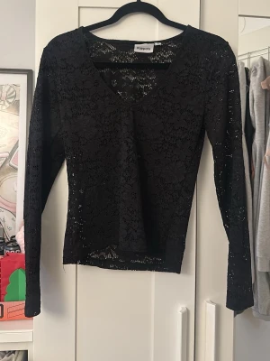 Svart spetsblus från Kappahl - Säljer en svart långärmad blus från Kappahl i genombruten spets med v-ringning. Blusen har ett blommigt spetsmönster och är lätt transparent, perfekt att styla med ett linne under. Superfin detalj till din outfit!