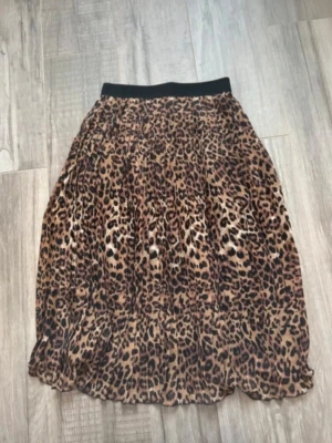 Plisserad leopardkjol med resårmidja - Säljer en plisserad kjol med leopardmönster och bred svart resår i midjan. Kjolen är i bruna och svarta toner och har ett tunt, lätt tyg med svart foder under. Perfekt för dig som vill sticka ut med en trendig look.
