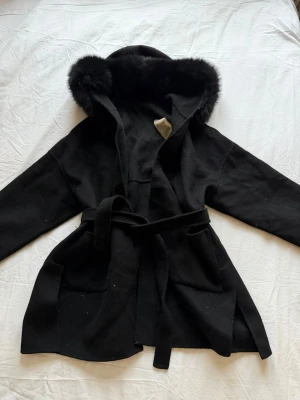 Svart kappa med pälskrage och bälte - Svart kappa med äkta  päls luva storlek S väl använd nopprig och samlats ludd även ens saken bandet sitter i har gått sönder så satt en säkerhetsnål luktar även rök  
