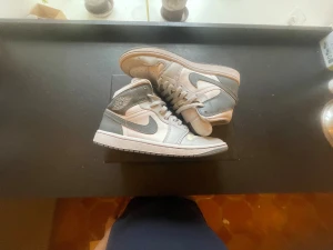 Nike Air Jordan 1 Mid grå/vit - Säljer ett par Nike Air Jordan 1 Mid sneakers i grått och vitt. Skorna har klassisk snörning, rund tå och platt sula. Ikonisk Jordan-logga på sidan och Nike Swoosh i grått. Tillverkade i skinn med snygga paneler och perforerad tå för extra stil.Lite creasade men ser knappast det när dem är på fötterna