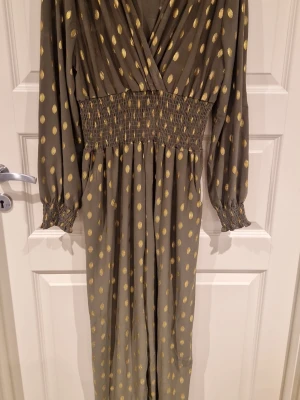 Grön byxdress med guldprickar Zanca Sonne - Säljer en grön byxdress från Zanca Sonne med glittriga guldprickar. Dressen har lång ärm, smock i midjan och vid ärmslut, omlott-ringning och ett flowigt, bekvämt tyg.Fickor. Perfekt för dig som gillar att sticka ut med coola detaljer och mönster.