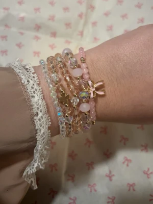 Handgjorda armband  -  armband med pärlor i rosa och transparenta toner, dekorerade med små guldfärgade detaljer och en rosett. 