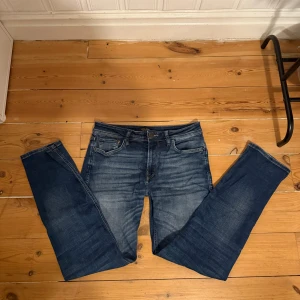 Blå jeans från Jack & Jones, 31/32 - Snygga blå jeans från Jack & Jones i klassisk femficksmodell. Jeansen är i Mörkblå tvätt med ljusare partier och läderpatch bak i midjan. Perfekta till vardagsstilen.