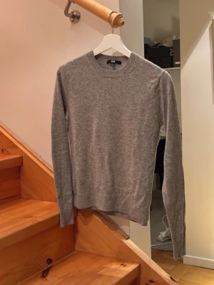 Grå cashmere tröja Uniqlo - Säljer en stilren grå stickad tröja från Uniqlo i storlek S. Perfekt för lager-på-lager och enkel att matcha med jeans eller chinos. Nypris ligger på 1499kr.