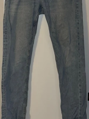 Blå jeans med rak passform - Säljer ett par klassiska blå jeans med rak passform. Jeansen har fem fickor och är tillverkade i ett slitstarkt denimtyg. Färgen är mörkblå med lätt tvättad look och de har en enkel design utan synliga detaljer eller mönster.