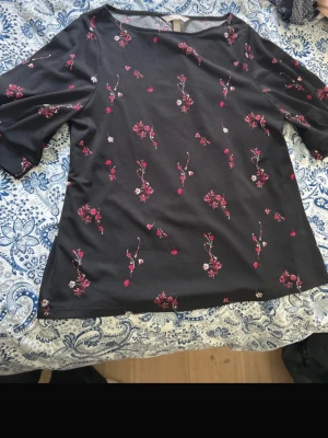Svart blommig blus från H&M - Svart blus från H&M med röda och vita blommor som mönster. Blusen har rund halsringning och halvlånga ärmar. Materialet känns mjukt och lätt, perfekt för vår och sommar. Snygg och enkel att matcha med jeans eller kjol.