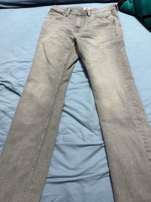 Grå jeans från 157, straight fit - Snygga grå jeans från 157 med klassisk femficksdesign och raka ben. Jeansen har en neutral grå färg och är tillverkade i mjukt denimtyg. Passformen är straight och de har bälteshällor samt knapp och dragkedja framtill. Perfekt för dig som gillar enkel och stilren look.