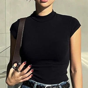 Svart polotopp med korta ärmar - Säljer en svart polotopp med korta ärmar och tight passform. Toppen har en hög krage och är gjord i ett mjukt, stretchigt material som sitter snyggt mot kroppen. Perfekt att matcha med jeans eller kjol för en clean och stilren look.