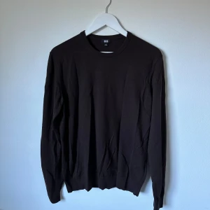 Mörkbrun ulltröja från Uniqlo, M - Mörkbrun, klassisk rundhalsad tröja från Uniqlo i 100% ull. Tröjan har långärmade ärmar och ribbade muddar vid hals, ärmslut och nederkant. Perfekt för dig som gillar stilrena och enkla plagg med skön passform. 3Y11