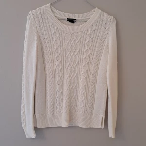 Vit kabelstickad tröja från Lindex - Vit kabelstickad tröja från Lindex med rund halsringning och snygga flätmönster framtill. Tröjan har ribbade muddar vid ärmslut och nederkant samt långärmad passform. Perfekt för lager-på-lager under kyliga dagar.