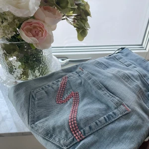 Ljusblå jeans från Nelly med rosa detaljer - Säljer ett par ljusblå jeans från Nelly med snygga rosa broderade sömmar på bakfickorna och vid knapphålen. Använd fåtal gånger