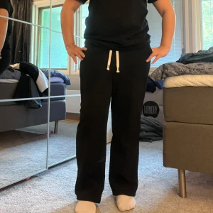 Svarta mjukisbyxor med manchester tyg och snörning - Svarta mjukisbyxor med manchester struktur och vit snörning i midjan. Byxorna har en rak och loose passform, är tillverkade i ett mjukt och stretchigt material som känns skönt mot huden. Perfekta för chill dagar eller när du vill vara extra bekväm.