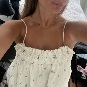 Vit blommig klänning  - Supersöt vit klänning med små blå blommor och tunna axelband. Klänningen har en rynkad, elastisk överdel och är luftig och flowy i modellen. Perfekt för varma dagar och ger en romantisk vibe med sitt blommiga mönster och lätta tyg. Aldrig använd då den tyvärr är i fel storlek!!