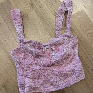 Rosa spetsig linnetopp från Amisu - Supersöt rosa linnetopp från Amisu med blommiga spetsdetaljer och 3D-rosor på axelbanden. Toppen är croppad och har en romantisk vibe med sitt tunna spetslager och mjuka tyg under. Perfekt för dig som vill sticka ut med en feminin look. Enda på plick som säljer en sån topp ✨❤️