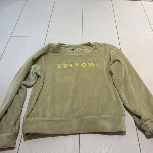 Gulgrön fleece-tröja med tryck - Mysig gulgrön fleece-tröja med texten YELLOW. framtill. Tröjan har rund halsringning och långa ärmar. Perfekt för dig som gillar en chill och skön stil med lite retrovibe.