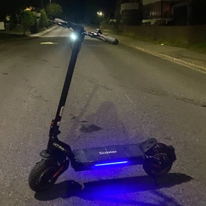 El sparkcykel iX7 Pro Scooter - Elektrisk sparkcykel iX7 Pro med LED-belysning, robust ram och stora däck för stabil körning. Snygg blå underbelysning och framljus för säkerhet på kvällen. Ser ut att vara i gott skick utan synligt slitage eller defekter. Perfekt för pendling eller fritid. 