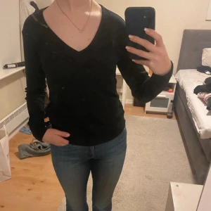 Svart v-ringad långärmad tröja - En stilren svart långärmad tröja med v-ringning. Tröjan har en klassisk passform och är perfekt att matcha med jeans eller kjol. Enkel och tidlös design som funkar året runt.
