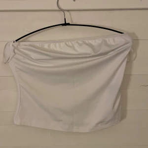 Vit bandeau tubtopp - Snygg vit bandeau tubtopp med enkel och stilren design. Toppen är axelbandslös och har en lätt glansig yta som ger en fräsch look. Perfekt att matcha med jeans eller kjol för en trendig outfit.