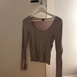 Beige långärmad topp  - En enkel och stilren beige långärmad topp från Gina Tricot. Toppen har rund halsringning och är tillverkad i ett tunt, mjukt bomullsmaterial. Perfekt att styla med jeans eller kjol för en clean look.