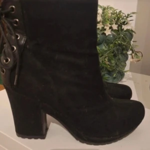 Svarta stövletter med snörning och klack - Snygga svarta stövletter med grov klack och snörning baktill. Skorna har dragkedja på sidan för enkel påtagning och är gjorda i mockaliknande material. Perfekta för dig som vill ha en edgy och trendig look.