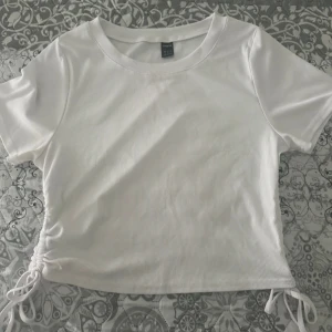 Vit ribbad topp med snörning från SHEIN - Vit ribbad topp från SHEIN i storlek XL. Modellen är croppad med korta ärmar och har snygg snörningsdetalj i sidan. Perfekt för dig som gillar enkel men trendig stil.
