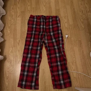 Pyjamasbyxor från Gina Tricot - Pyjamasbyxor från Gina Tricot i mjukt bomullstyg. Byxorna har snörning i midjan och ett avslappnat, rakt snitt. Perfekta för chill dagar hemma eller som mysbyxor. Klassisk rutig design i rött, svart och vitt. En liten fläck som inte syns knappt